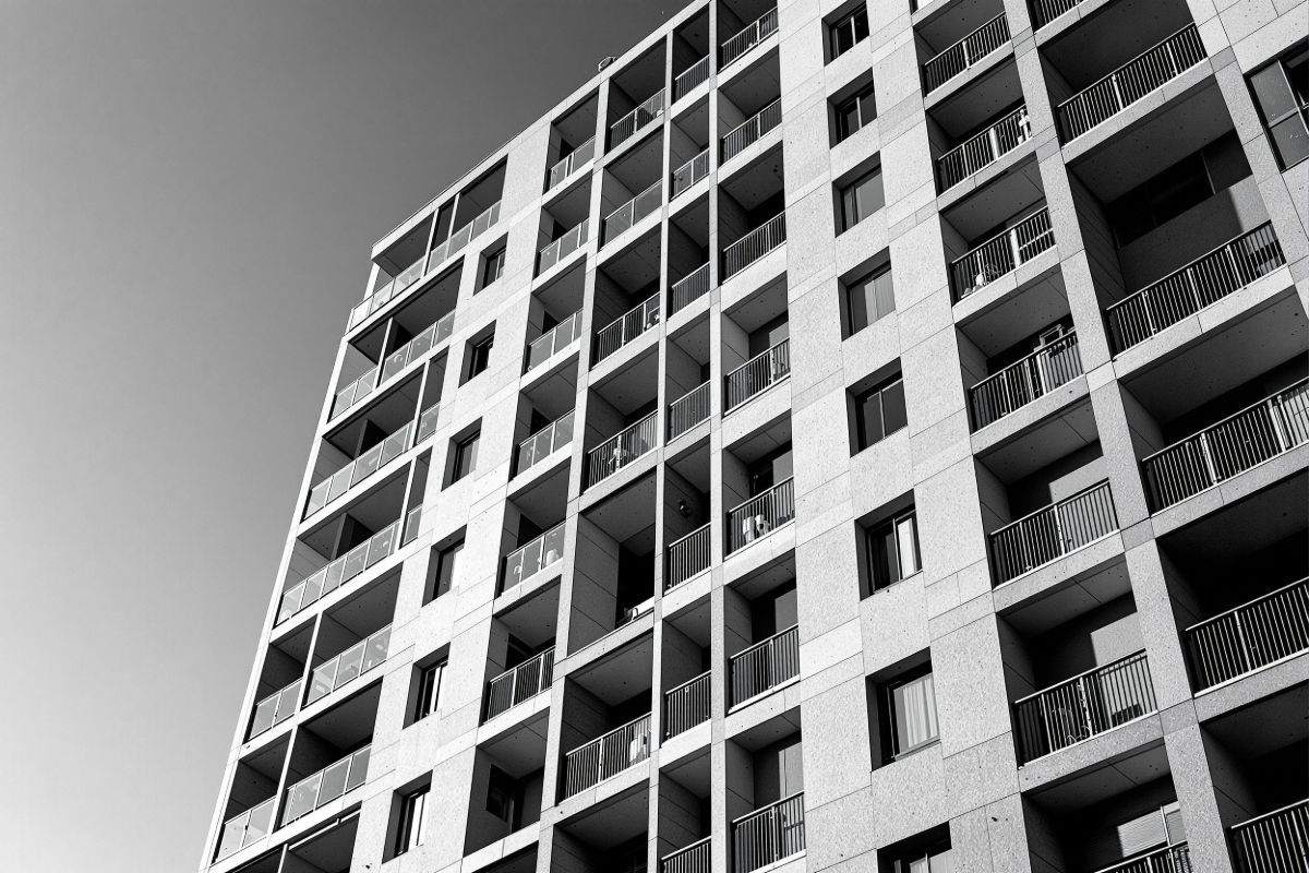 Fachada de un edificio de viviendas recién terminado en ángulo bajo, con la
            retícula de balcones marcada por la luz rasante de la tarde.