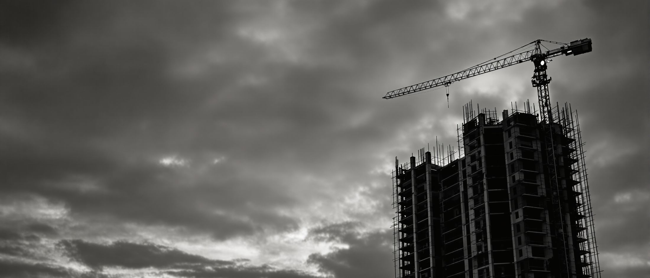 Estructura de un edificio de viviendas en construcción al anochecer, con la
        silueta de una grúa torre recortada contra el cielo.